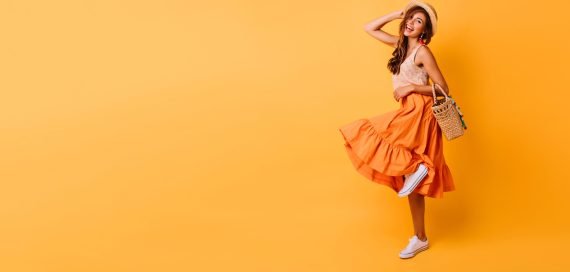 Magnificent woman in long bright skirt dancing in studio. Carefree inspired female model posing with pleasure on yellow background.